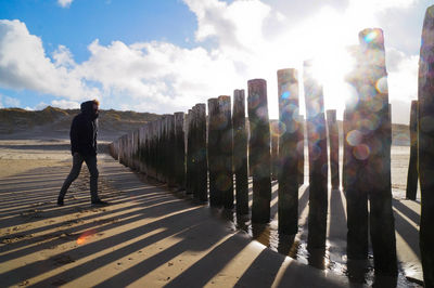 Man walking by wooden post at beach against sky