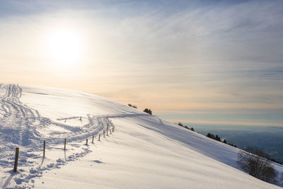 Snow covered land against sky during sunset