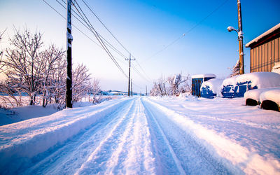 Snow covered road by trees against sky