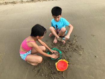 High angle view of siblings playing with toys on sand at beach