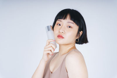 Portrait of young woman holding hat against white background