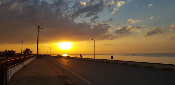 Road by sea against sky during sunset