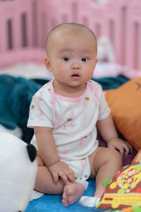 Portrait of cute baby boy sitting on bed at home