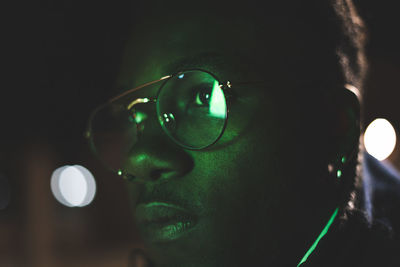 Close-up of man wearing eyeglasses in illuminated city at night