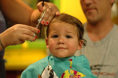Portrait of toddler boy getting hair cut with father in salon
