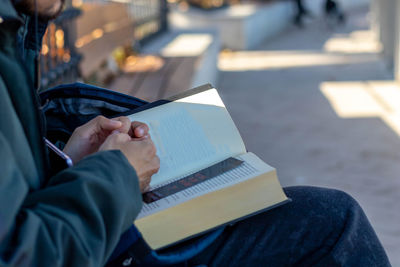 Young man reading a book sitting on a bench in a park