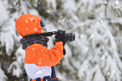 Close-up of boy holding camera during snowfall