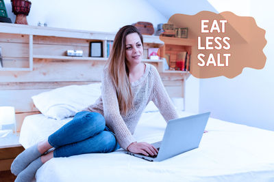 Young woman using phone while sitting on bed at home