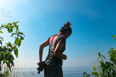 Woman standing by plants against blue sky