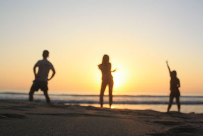 Silhouette people on beach against clear sky during sunset