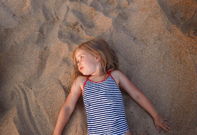 High angle view of girl looking away while lying on sand