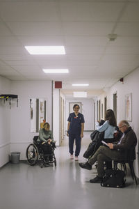 Smiling female nurse talking to patient sitting in corridor at healthcare center