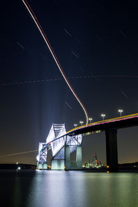 Illuminated bridge over river against sky at night