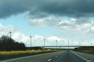 Road passing through field against cloudy sky