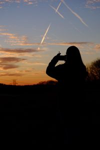 Silhouette of woman photographing against sky during sunset
