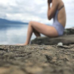 Midsection of man sitting on shore at beach against sky