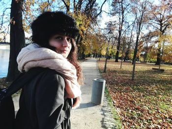 Portrait of smiling young woman standing by trees during autumn