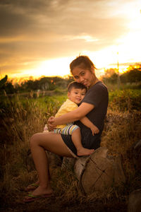 Portrait of happy mother and son on field against sky during sunset
