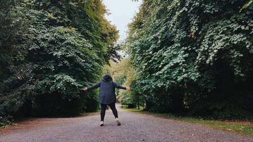Rear view of woman with arms outstretched on footpath amidst trees