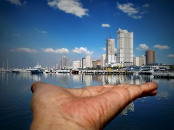 Cropped image of hand holding sea against buildings in city