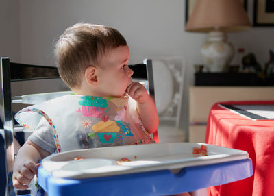 Cute toddler having tomatoes in his high chair for lunch