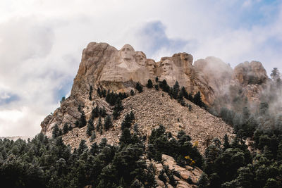 Low angle view of rocks on mountain against cloudy sky