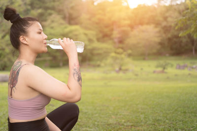 Side view of young woman drinking water bottle on field