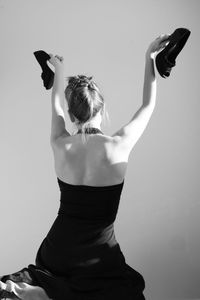 Rear view of woman holding shoes against white background