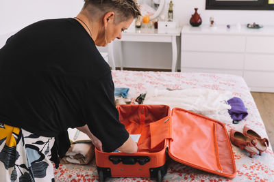 Rear view of woman packing bag at home