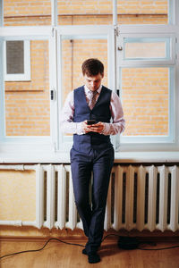 Full length of young man using phone while standing on building