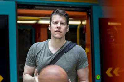 Portrait of young man with basketball standing at train entrance