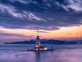 Lighthouse by sea against sky during sunset