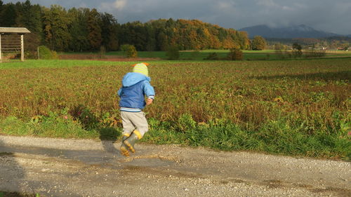 Rear view of boy jumping on puddle by field
