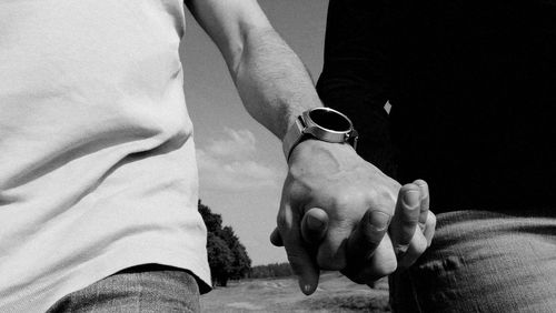 Midsection of couple holding hands while standing on field