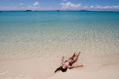 Woman in bikini relaxing at beach against sky