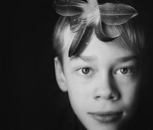 Close-up portrait of boy wearing flower against black background