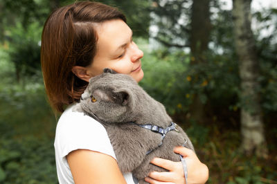 Young woman holds and gently hugs her pet grey shorthair british cat