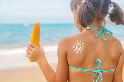 Rear view of girl with flower made with suntan lotion at beach