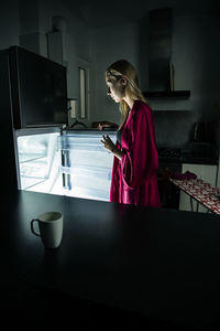 Side view of woman opening refrigerator door in kitchen