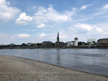 View of buildings by river against cloudy sky