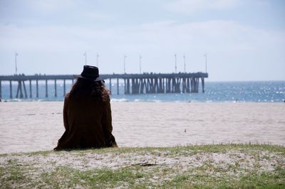 Rear view of woman sitting at beach against sky