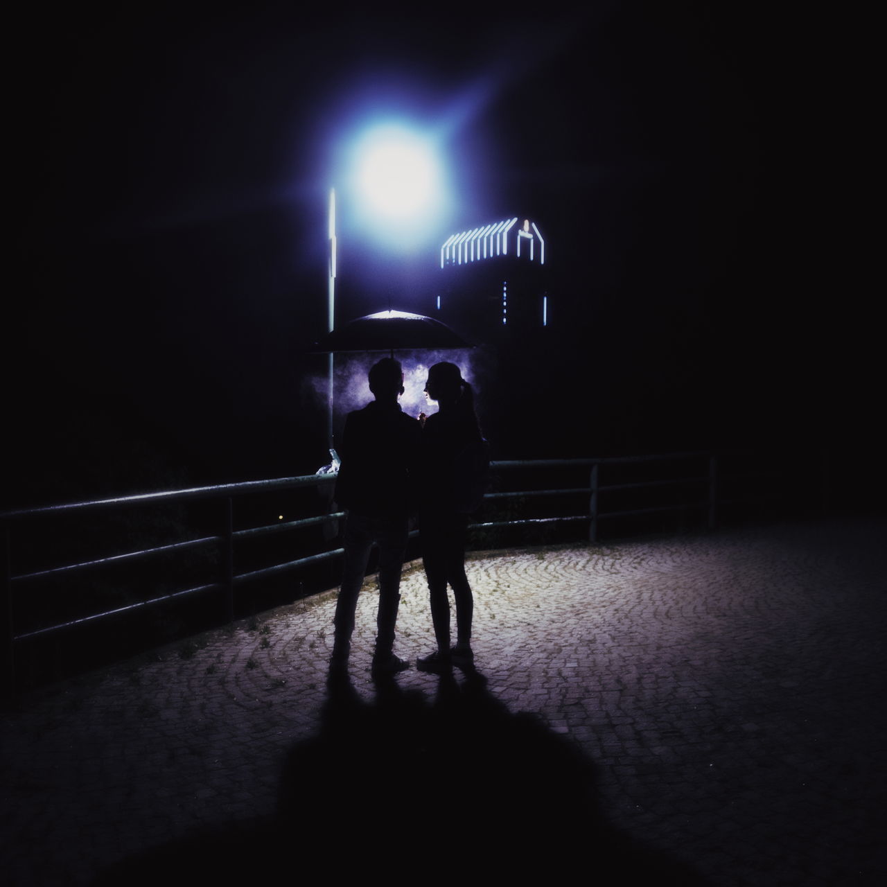 MEN STANDING ON ILLUMINATED RAILING