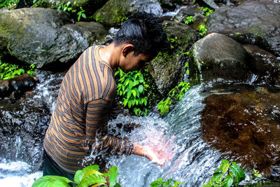 Young man standing by flowing water in forest