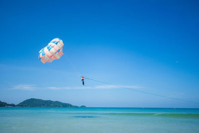 Person paragliding over sea against blue sky