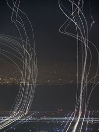Light paintings over illuminated airport by river in city against sky at night