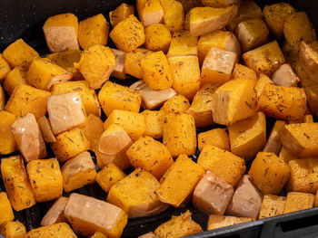 Close-up of healthy butternut squash in cubes in an air fryer with herbs.