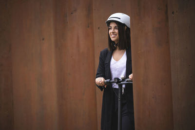 Portrait of young woman looking away while standing against wall