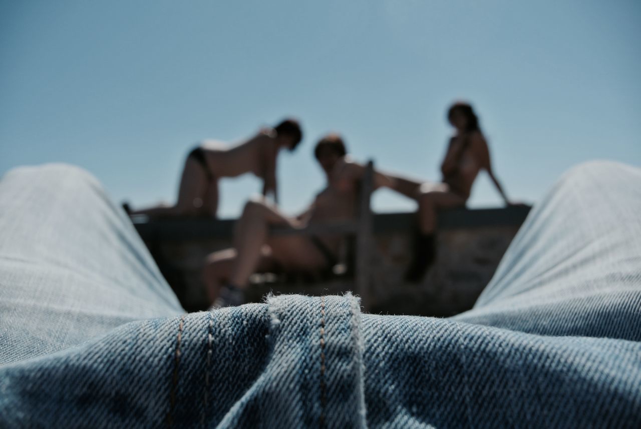 clear sky, men, lifestyles, leisure activity, focus on foreground, copy space, togetherness, day, selective focus, person, outdoors, sky, sunlight, sitting, unrecognizable person, built structure, rear view