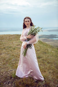 Woman stands on a mountain cliff in a pink long dress in summer