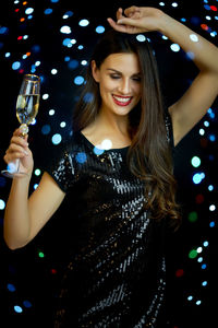 Smiling woman having champagne against illuminated lighting equipment